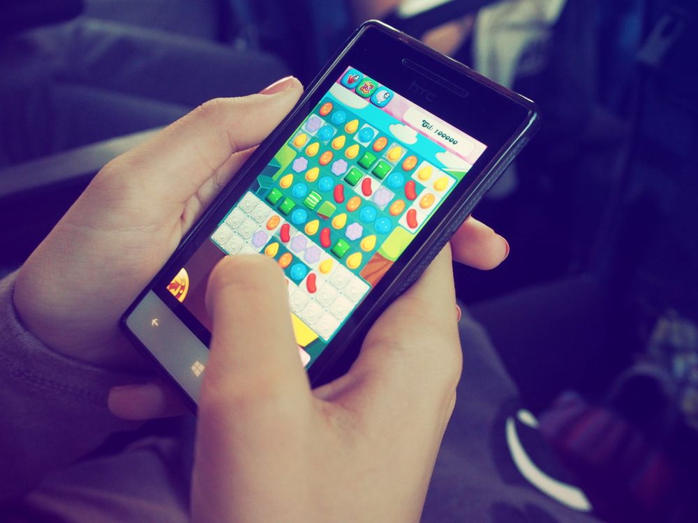 Tangan memegang smartphone dengan permainan berwarna-warni di layar